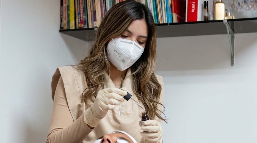 Cosmetóloga con mascarilla aplicando un sérum facial con cuentagotas